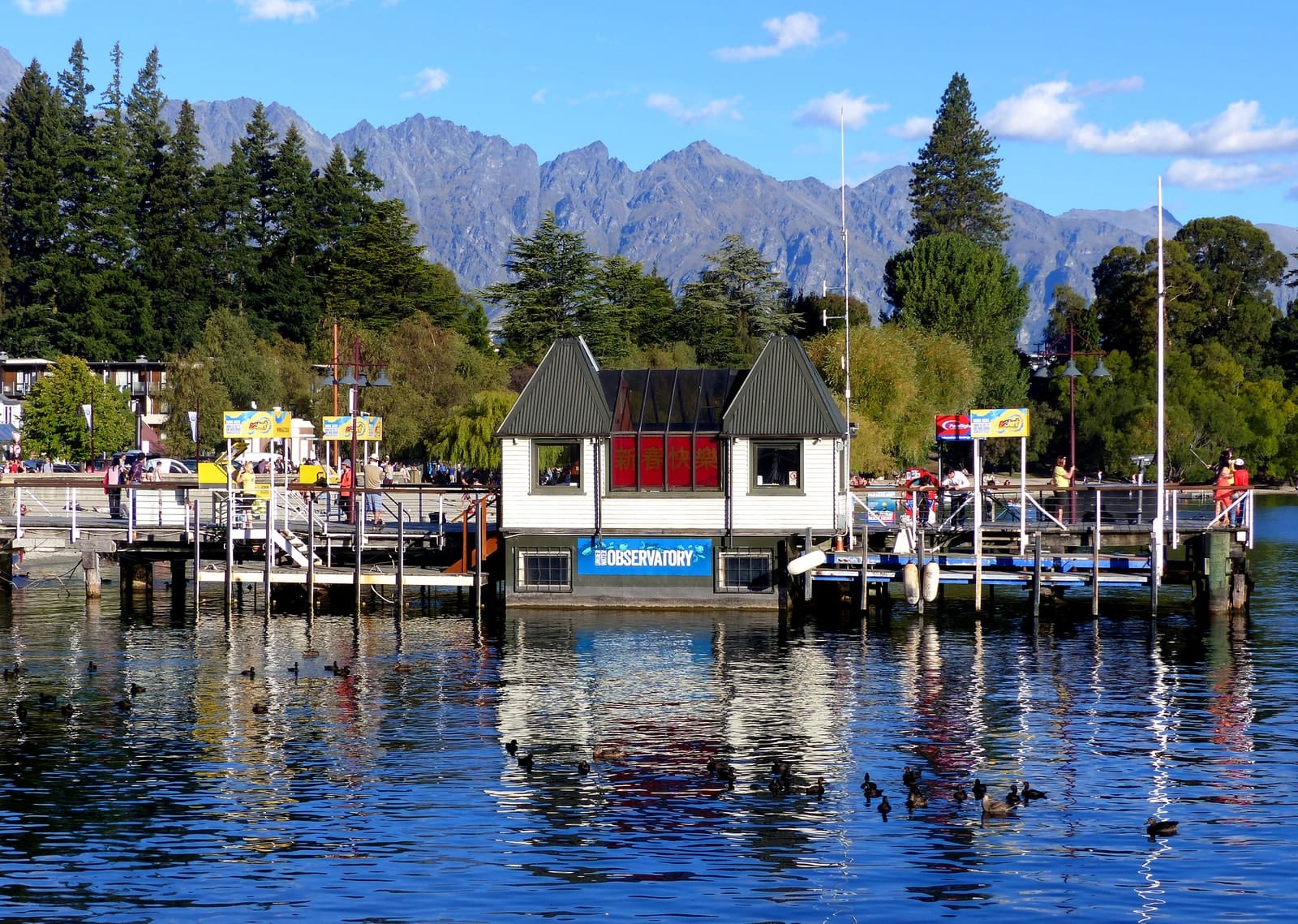 Visitors and a pier building at Queenstown waterfront with mountains behind